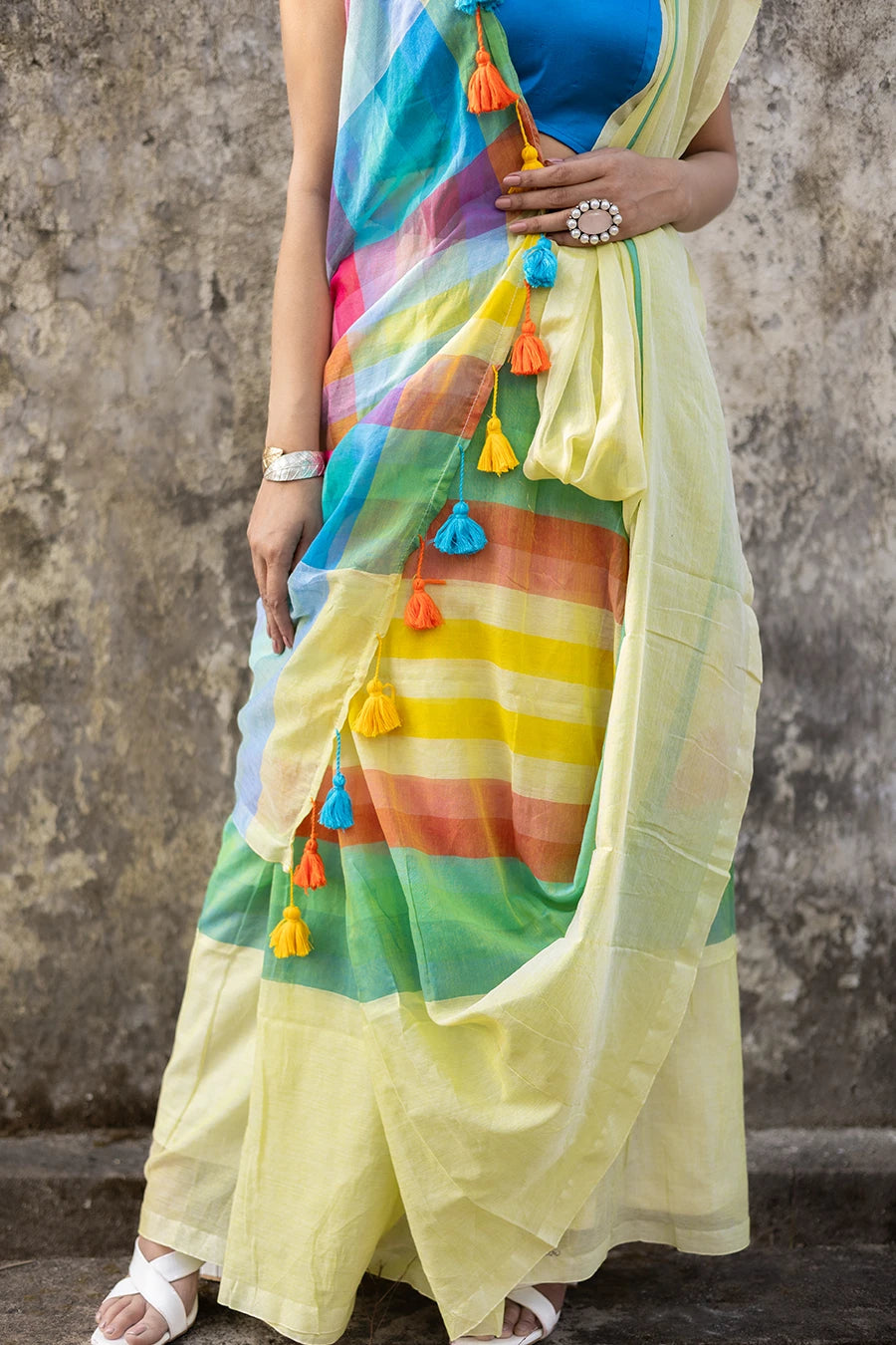 Woman wearing a colorful saree with a blue blouse against a textured wall.