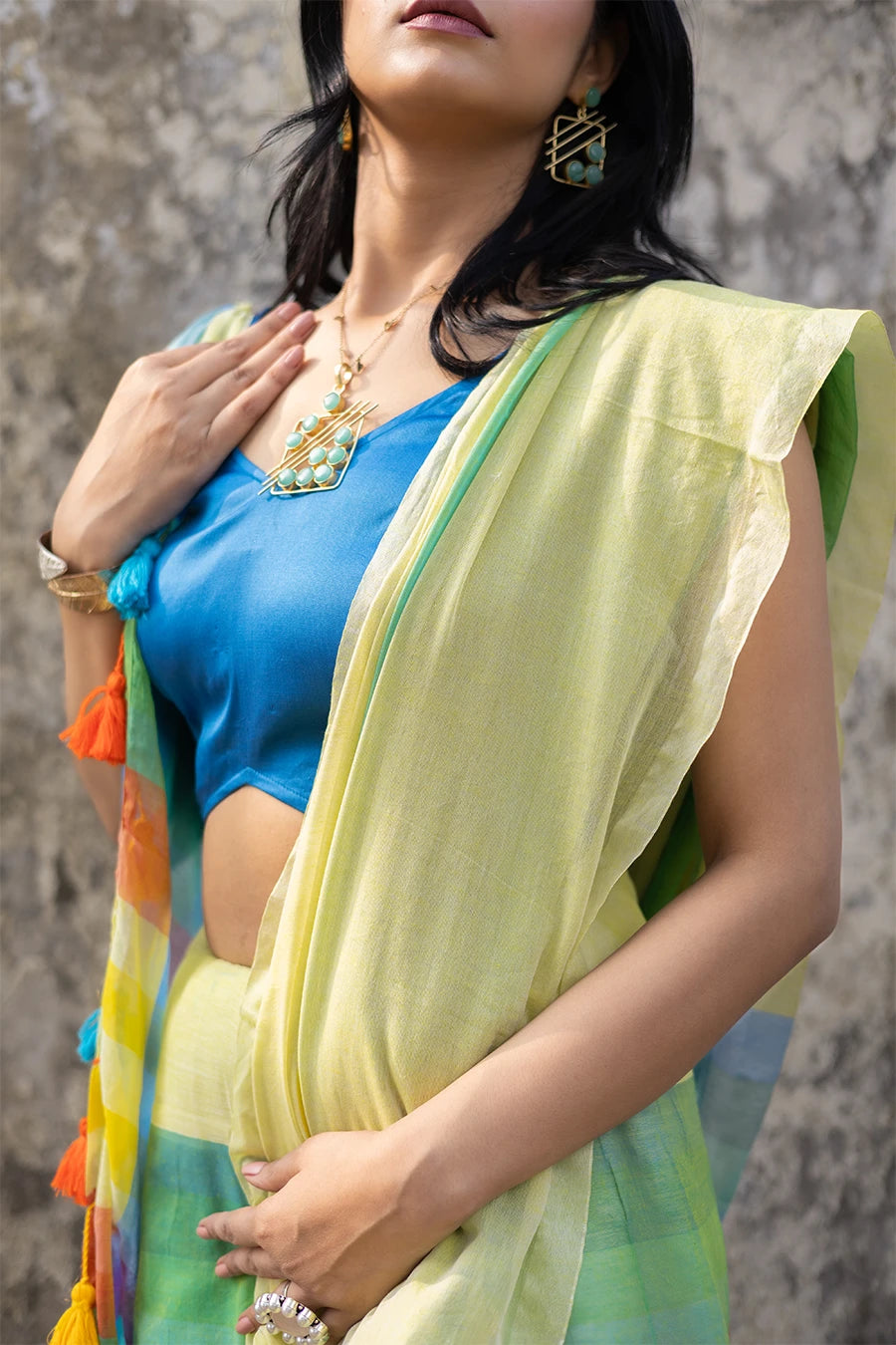 Woman wearing a colorful saree with a blue blouse against a textured wall.