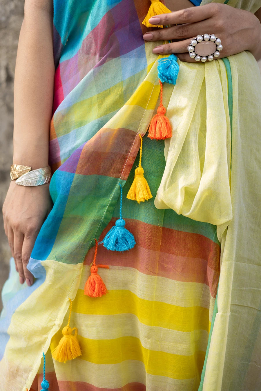 Woman wearing a colorful saree with a blue blouse against a textured wall.
